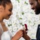 cheerful african american bride looking at box with ring near happy bridegroom and flowers