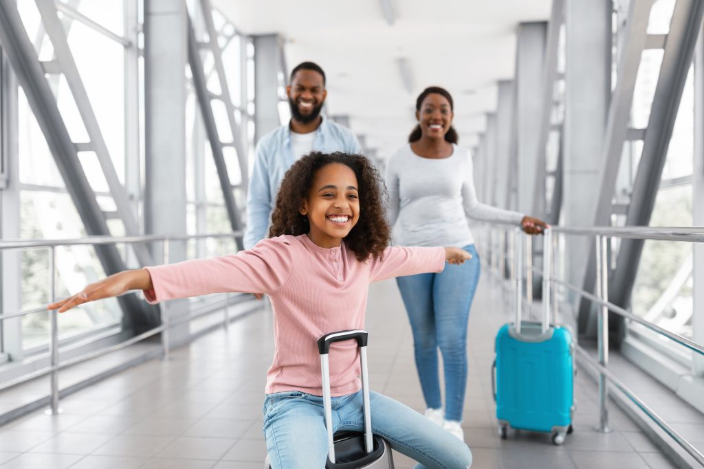 happy black family traveling with kid, girl playing in airport